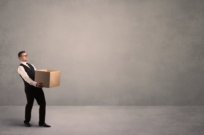 A well dressed young office worker holding an empty paper box with clear concrete wall background concept.