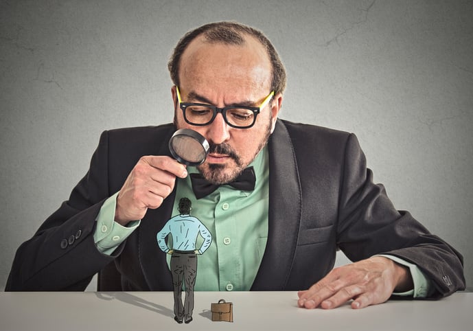 Curious corporate businessman skeptically meeting looking at small employee standing on table through magnifying glass isolated office grey wall background. Human face expression, attitude, perception