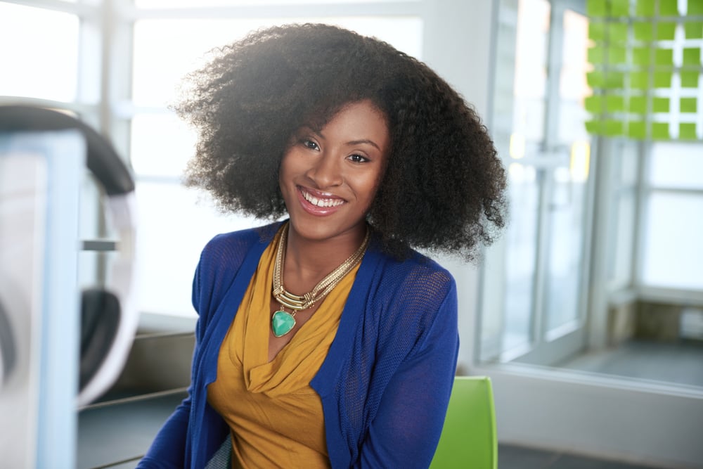 Portrait of a smiling woman with an afro at the computer in bright glass office